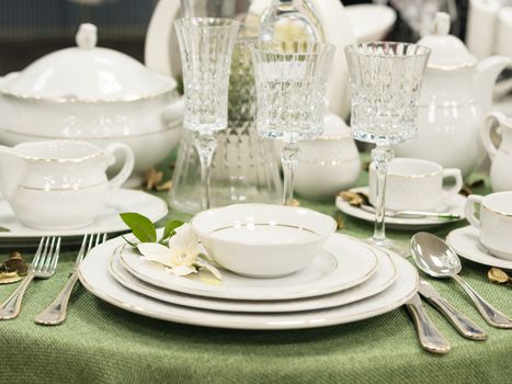 Set of new dishes on table with green tablecloth. Stack of white plates with flowers on restaurant table. Shallow DOF