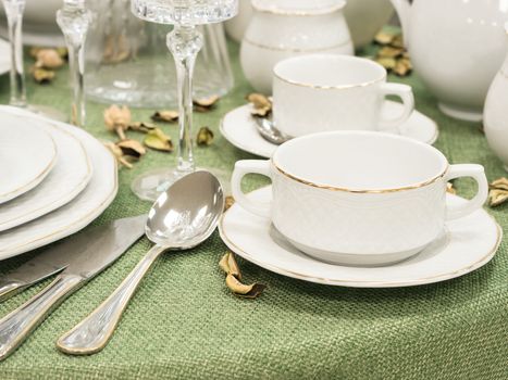 Set of new dishes on table with green tablecloth in restaurant