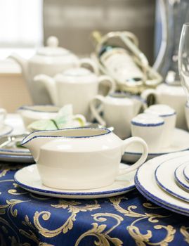 Set of new dishes close up on table with blue tablecloth. Saucer, plates, teapots, wine bottle on table. Shallow DOF. Vertical