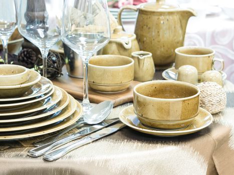 Set of new dishes on table with tablecloth. Stack of beige plates and wine glasses on restaurant table. Shallow DOF