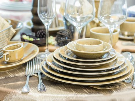 Set of new dishes on table with tablecloth. Stack of beige plates and wine glasses on restaurant table. Shallow DOF