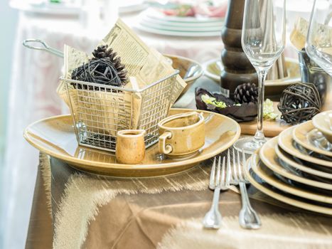 Set of new dishes on table with tablecloth. Stack of beige plates and wine glasses on restaurant table. Shallow DOF