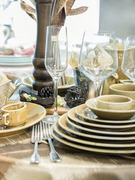 Set of new dishes on table with tablecloth. Stack of white plates and wine glasses on restaurant table. Shallow DOF. Vertical