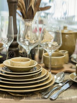 Set of new dishes on table with tablecloth. Stack of white plates and wine glasses on restaurant table. Shallow DOF. Vertical