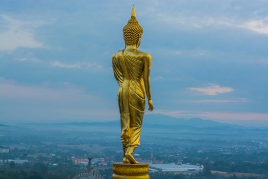 Buddha statue facing cityscape in morning sunrise on mountain top in Nan provincial town, Northern Thailand.