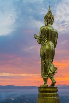 Buddha statue facing cityscape in morning sunrise on mountain top in Nan provincial town, Northern Thailand.