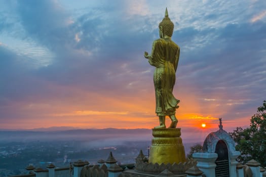 Buddha statue facing cityscape in morning sunrise on mountain top in Nan provincial town, Northern Thailand.