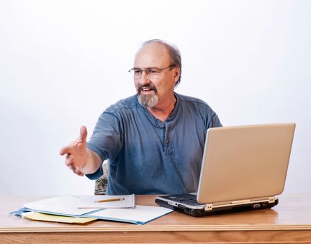 Casual dressed businessman reaches to shake the hand of a client across his desk.