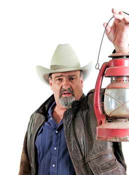 Mature cowboy looking forward by light of his handheld kerosene lantern. Isolated on a white background.