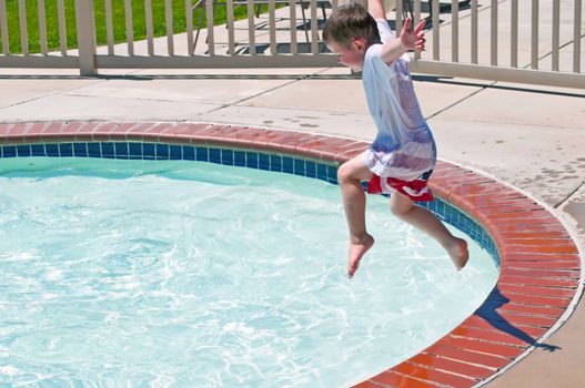Exuberant little boy jumping into the water having fun at the local swimming pool.