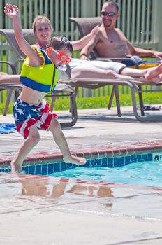 Happy young couple watch their little boy jumping into the water at the swimming pool.