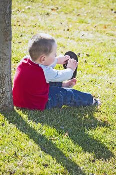 Cute little boy putting his flip-flops back on under a miniture shade tree.