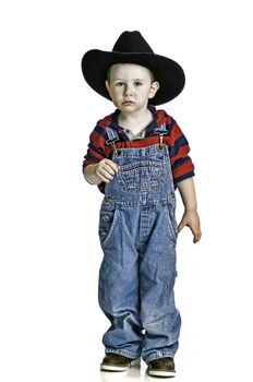 Cute little boy in his cowboy hat and cover-alls with a serious look on his face.