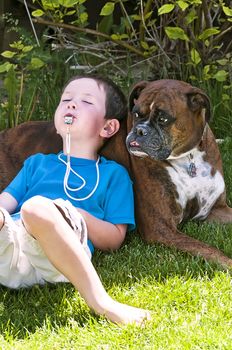 Little boy rest against his pet Boxer dog after playing in the yard with a whistle.