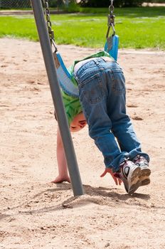 Cute little boy laying on his stomach in a swing while playing in the sand below.