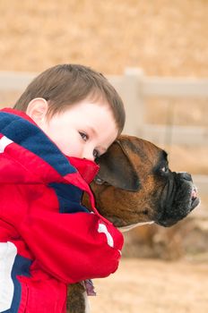 Little boy hugging his best freind, the family pet Boxer. After playing hard in the back yard two pals stop to rest.