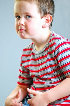 Cute little boy putting on his best tough guy look against a grey background.