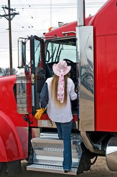 A woman truck driver enters the cab of a big rig.