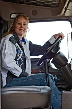 Woman truck driver sitting in the drivers seat of a semi-truck.