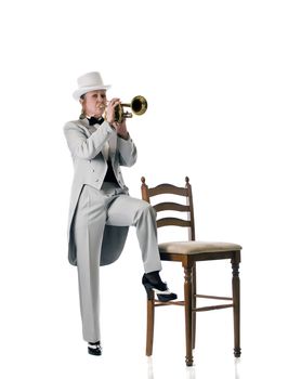 Pretty blonde woman in tuxedo and top-hat playing a trumpet standing next to a stool.