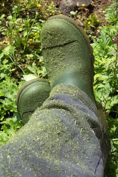 Urban farmer green gardering boots above garden background
