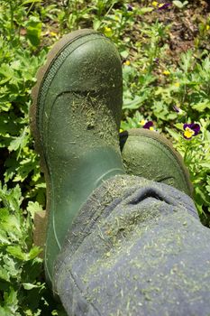 Urban farmer green gardering boots above garden background