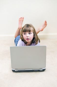 Cute little girl daydreaming while playing on a laptop computer.