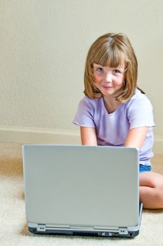 Cute little girl looks up and smiles from the computer game she is playing on a laptop while seated on the floor.