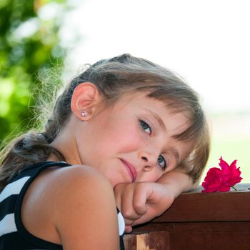 Cute little girl resting her head on the porch rail after playing hard.