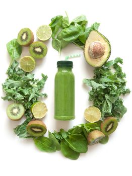 Bottled green smoothie surrounded with fruits and vegetables including spinach kale and avocado