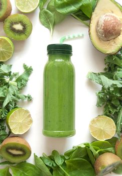 Bottled green smoothie surrounded with fruits and vegetables including spinach kale and avocado