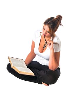 Pretty young girl reading a book while seated cross-legged. Isolated on a white background