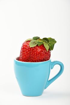 Healthy alternative, one big red ripe mellow strawberry in small blue espresso coffee cup over white background, close up, side view
