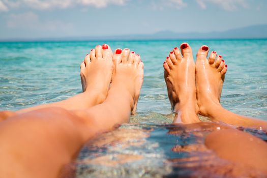 Two girlfriends enjoying on the beach. They are lounging with legs in the sea. Close-up on the womans legs.