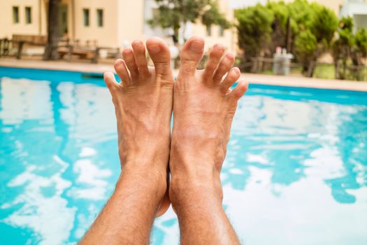 Young man relaxing nex to swimming pool. Close-up of a man's legs.