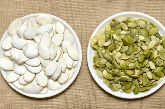 Two plates of peeled and in-shell pumpkin seeds, stands on the old boards.