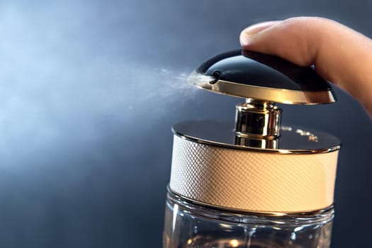 Close up of spraying perfume bottle on a dark grey background