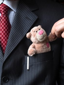 The elegant stylish businessman keeping cute teddy bear in a his breast suit pocket. Formal negotiations concept