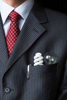 The elegant stylish businessman keeping two different light bulbs - Incandescent and fluorescent energy efficiency - in his breast suit pocket. Energy saving concept. Environment protection theme
