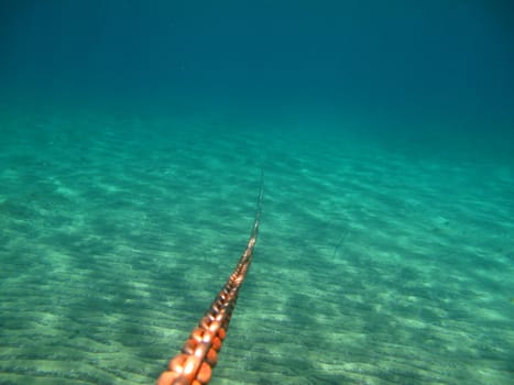 Worn Iron Anchor Chain shot from underwater to surface. Blue Background. Shallow Depth of Field.