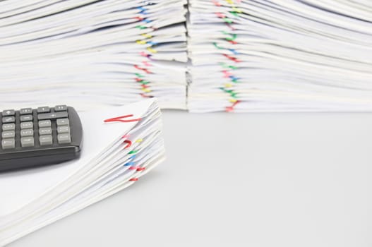 Black calculator place on pile of document have blur overload of paperwork with colorful paperclip on white background.