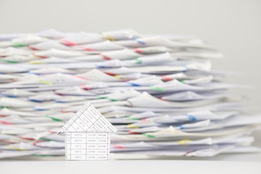 House on white table have blur stack overload of paperwork with colorful paperclip as background.