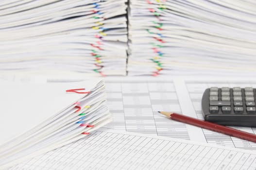 Pile of document on finance account have blur brown pencil with black calculator and overload of paperwork with colorful paperclip as background.