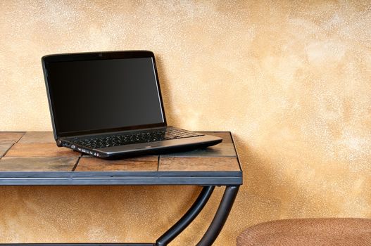 Laptop computer against a textured wall on a small table. Clipping path around the screen to add your own graphics.