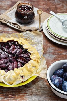 Rustic pie with plums and plum jam on wooden background