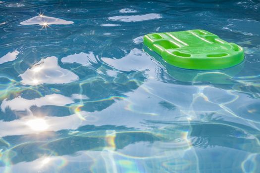 Green lifesaver floating in a swimming pool in summer time with sun reflection