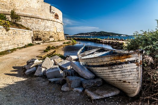 aged and abandoned fishing boats laying on the shore closed to a old tower in france
