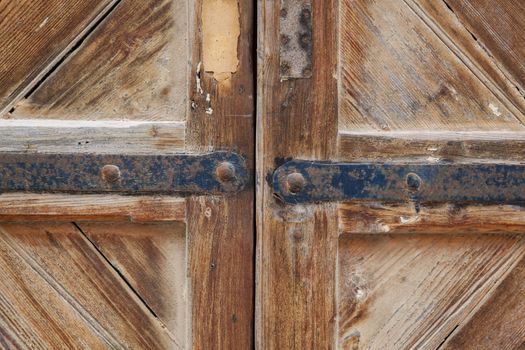 Portion of a weathered wood brown door with his hinges