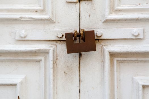 A withe wood door closed with a weathered rusty lock