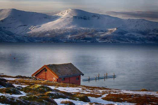 An isolated house on a lake between snowy mountains